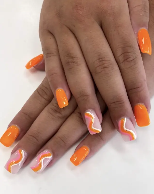 Bright orange gel nails with pink and gold swirl art