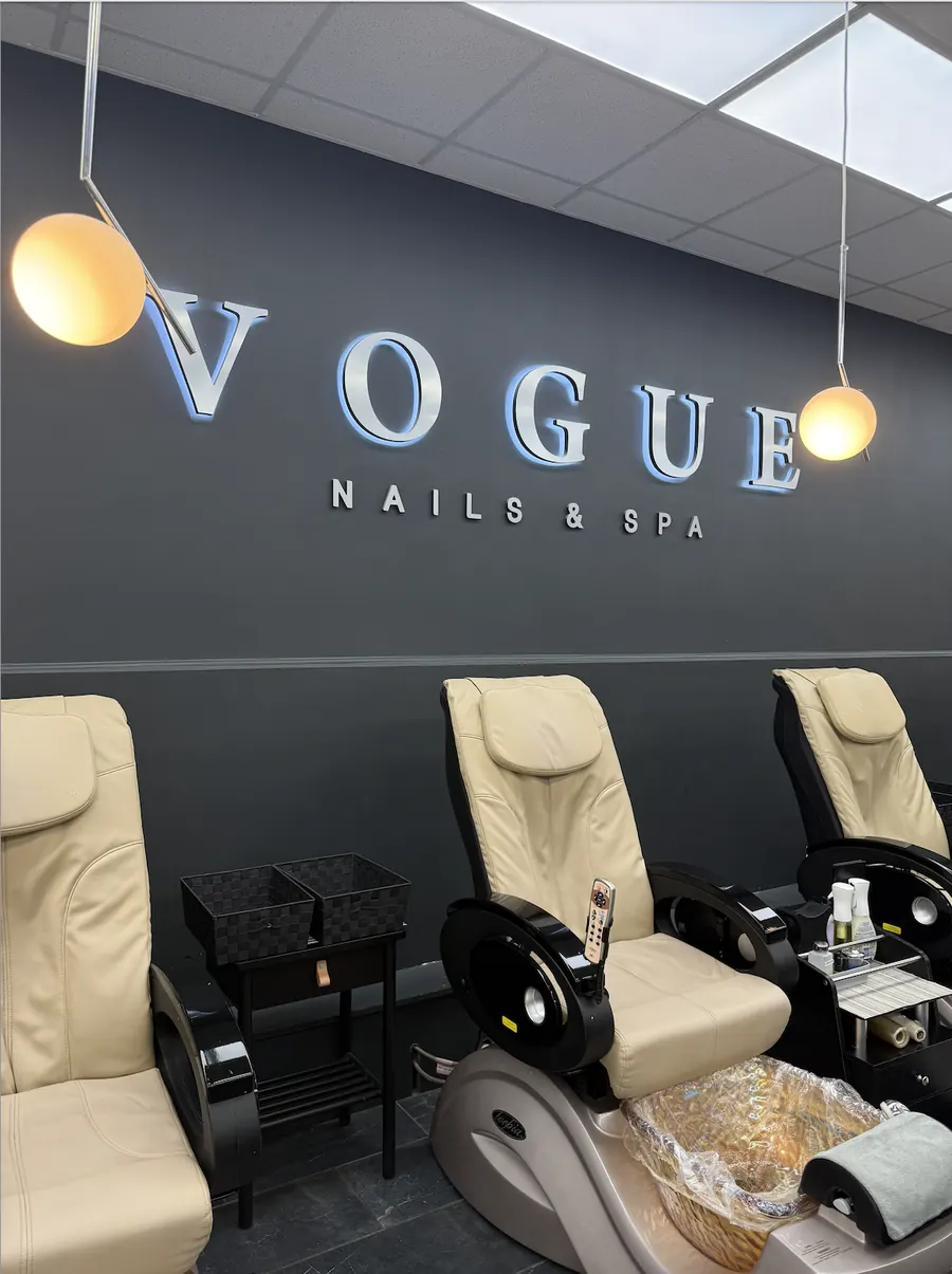 Massage pedicure chairs beneath the illuminated Vogue Nails & Spa sign